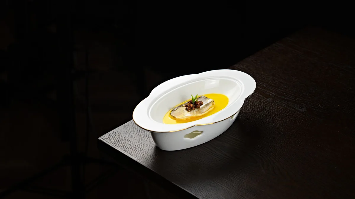 Tigela branca com sopa quente fumegante e colher ao lado sobre mesa de madeira