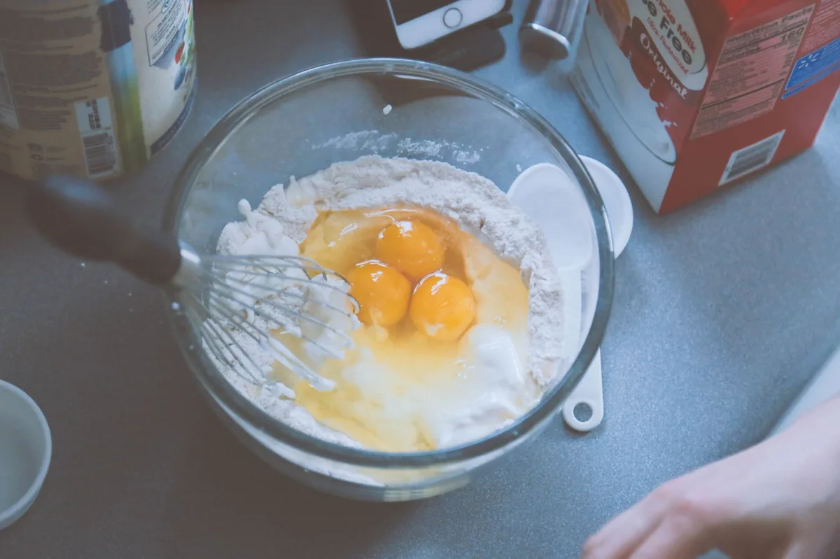 Mãos mexendo ingredientes em tigela com colher de pau, representando técnicas de preparo na cozinha