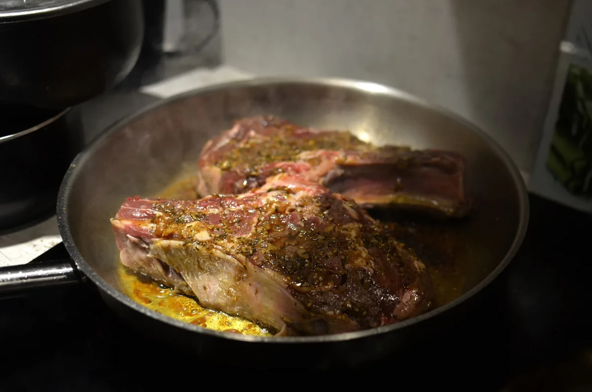 Bife de carne vermelha sendo frito em frigideira quente