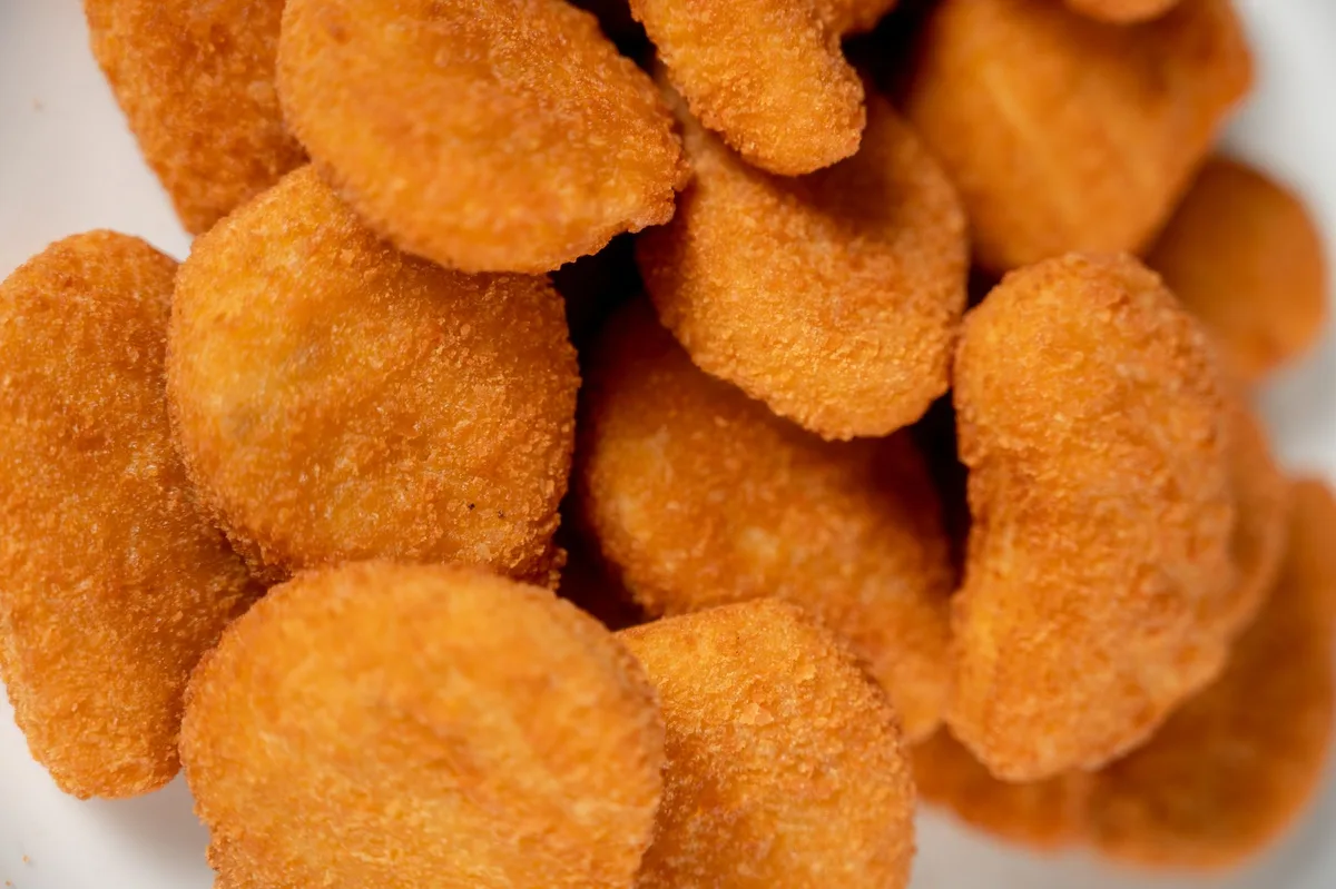 Pedaços de carne empanada fritando em frigideira quente com óleo dourado