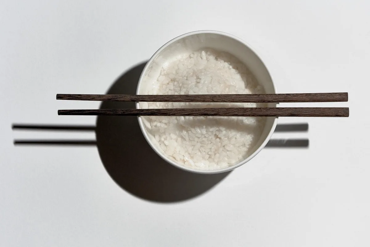 Frigideira com arroz branco pronto sendo segurada sobre o fogão