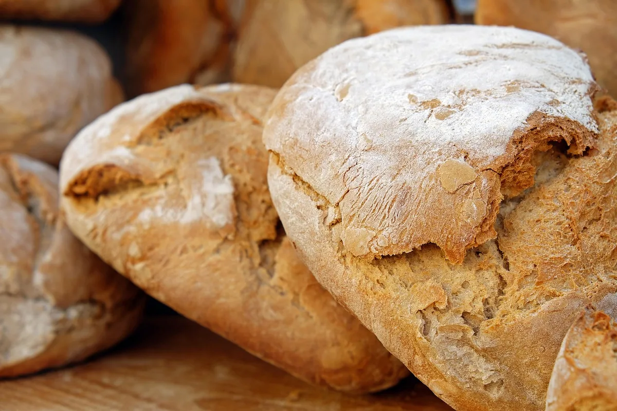 Pão caseiro assado com crosta dourada sendo segurado pelas mãos