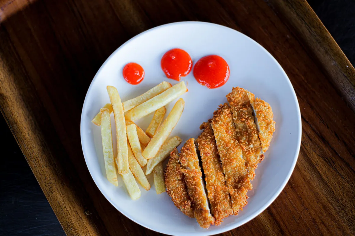 Bife empanado dourado fritando em frigideira de inox
