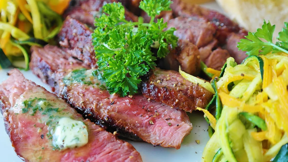 Bife de carne bovina sendo grelhado em frigideira quente com gordura dourada.